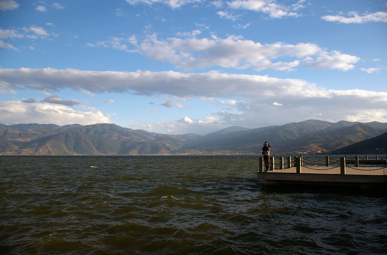 Qionghai Lake in Xichang, with mountain slopes, clouds and a lakefront viewing platform.
