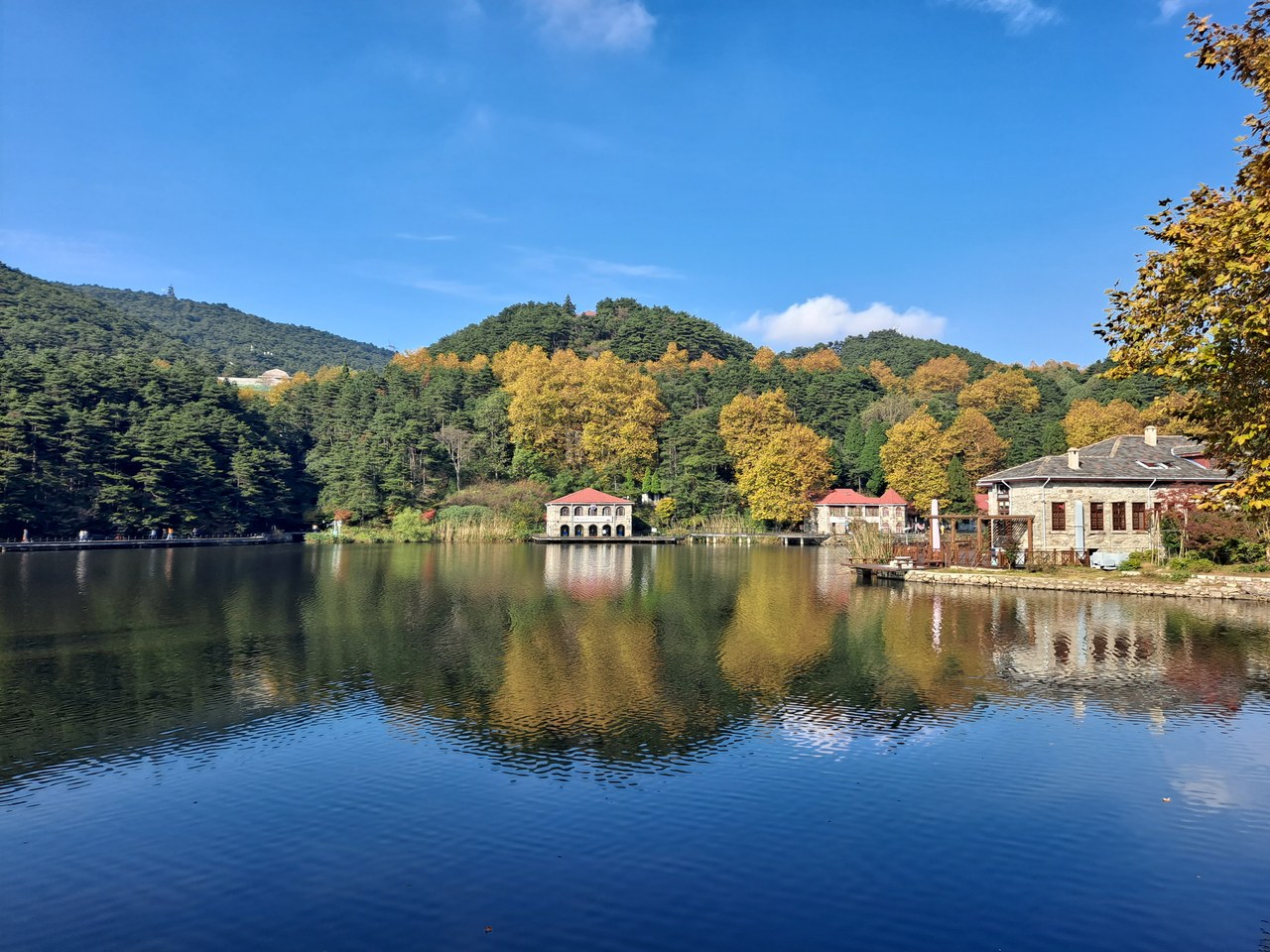 Ruqin Lake on Lushan reflects wooded slopes, autumn-coloured trees and lakeside pavilions under a blue sky.