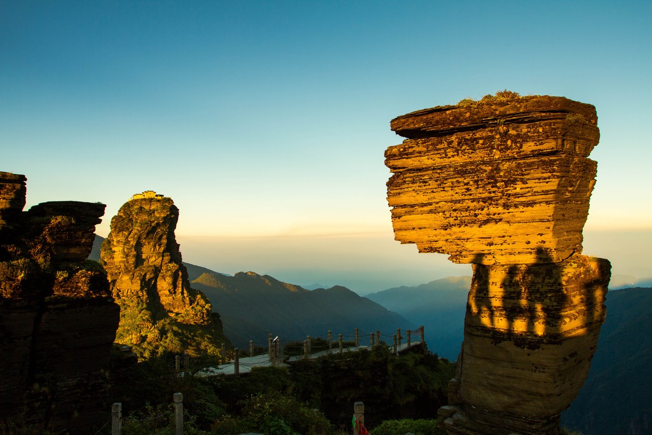 The layered Mushroom Stone rock formation above forested ridges at Fanjingshan, lit by low sunlight.