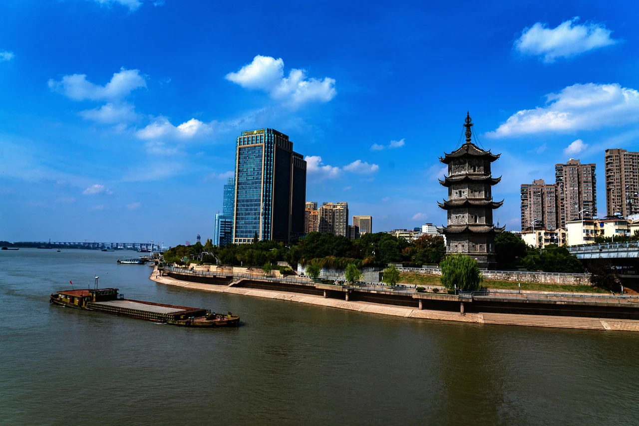 Zhongjiang Pagoda beside the water in Wuhu, with a curving embankment, city buildings and blue sky.