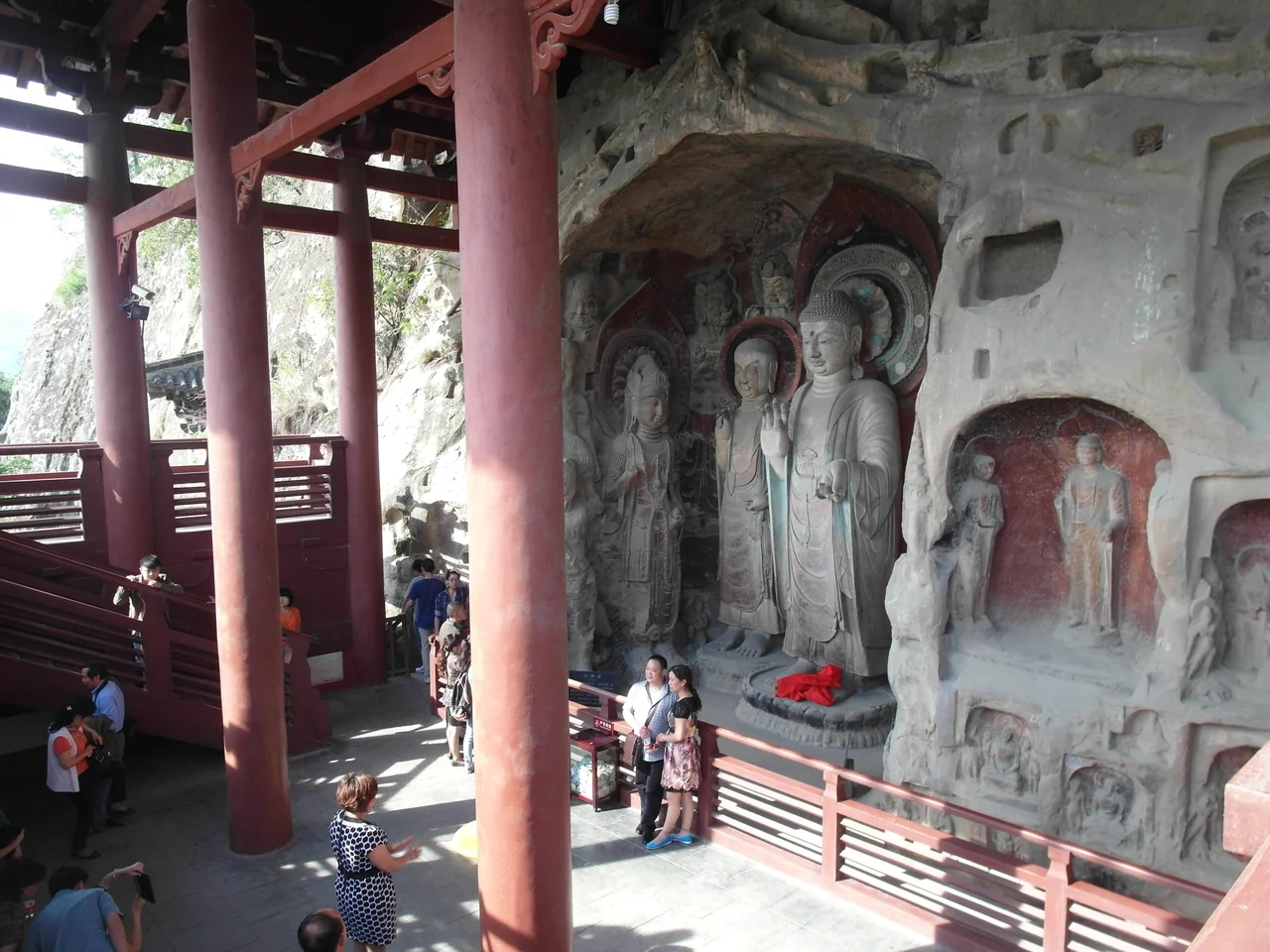 Buddhist cliff carvings beneath a red-columned shelter at Huangze Temple in Guangyuan, with visitors beside the railing.