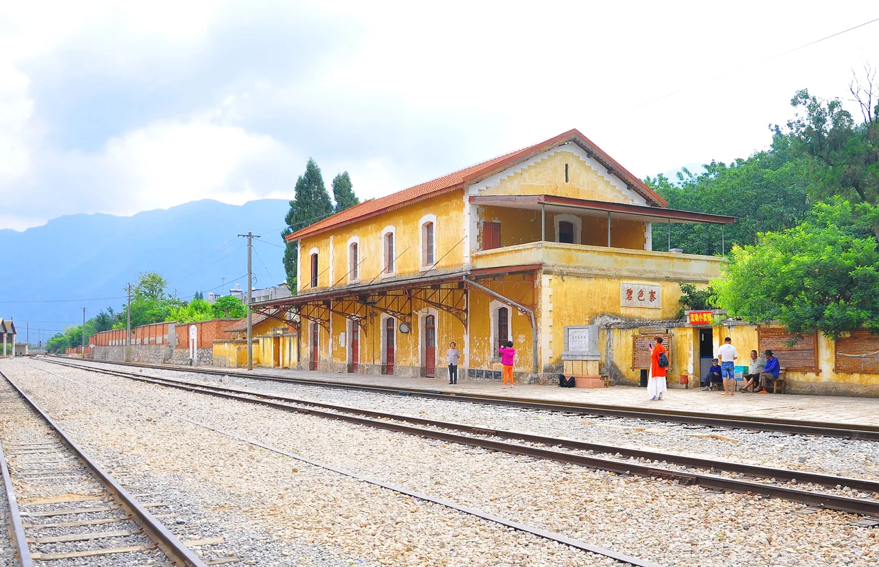The yellow Bisezhai station building beside railway tracks, with the Bisezhai name on its wall and mountains behind.