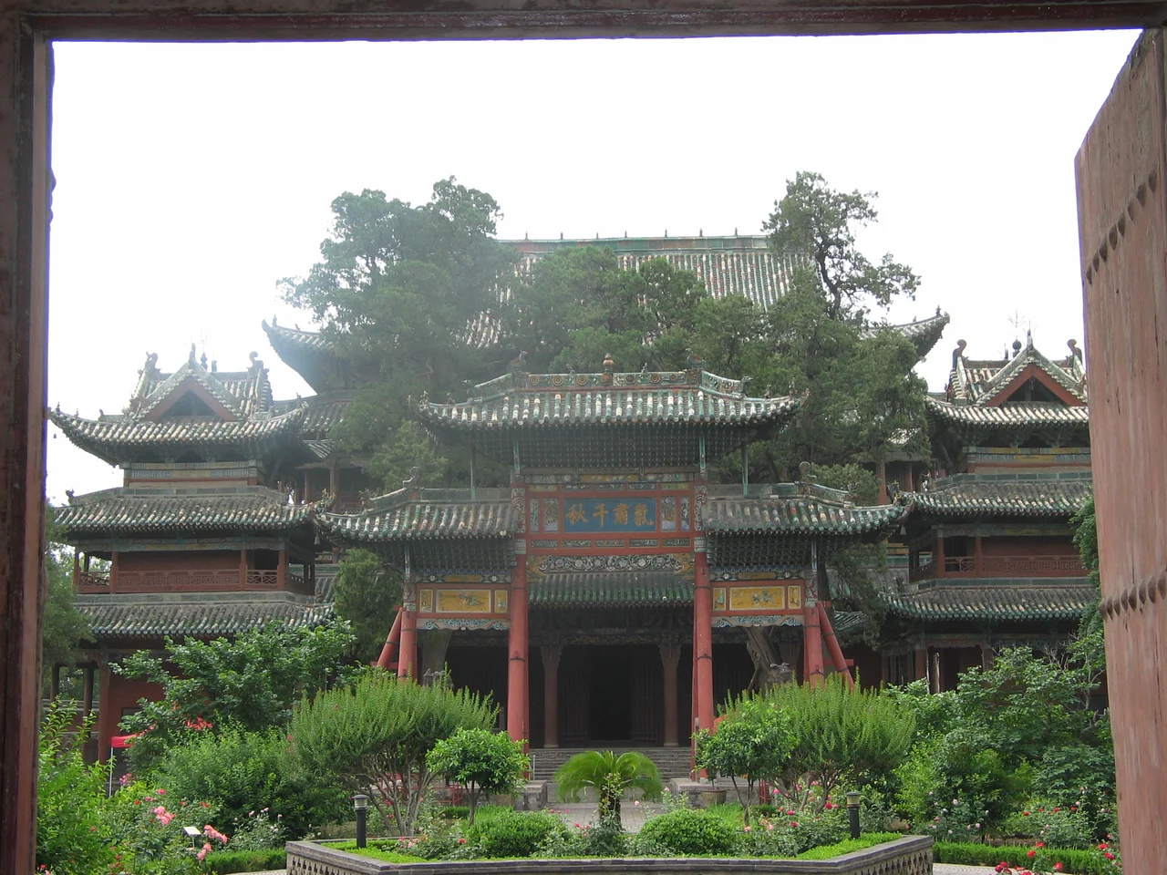 The ornate green-tiled Spring and Autumn Building at Jiezhou Guandi Temple, seen through a gateway above the garden.