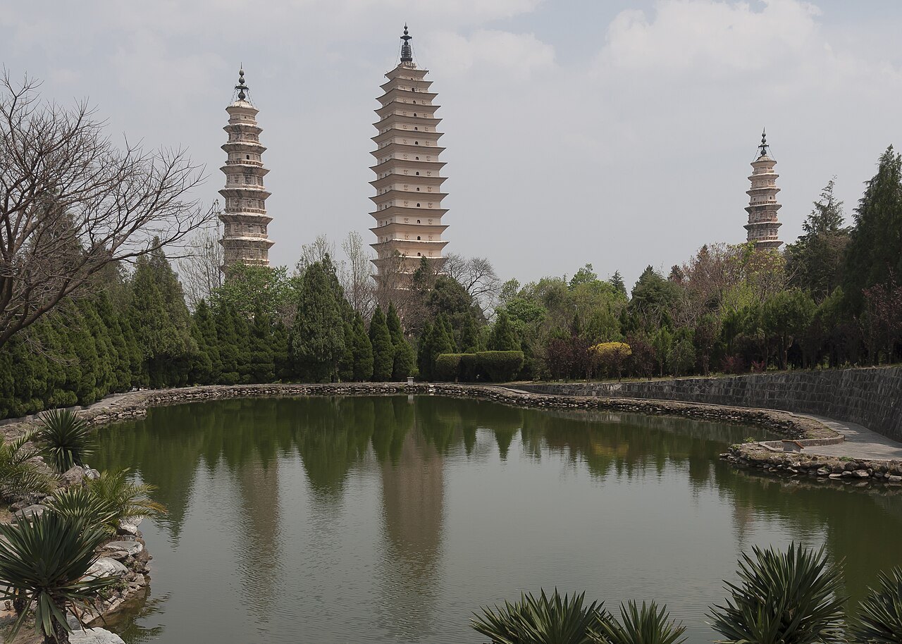 Three pagodas of different heights rising above trees and a reflecting pool in Dali.