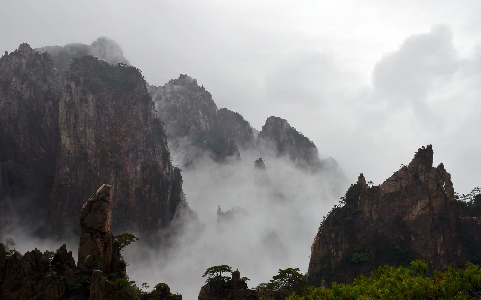 Granite cliffs and pine-covered rock spires rising through mist in Huangshan’s West Sea Grand Canyon.