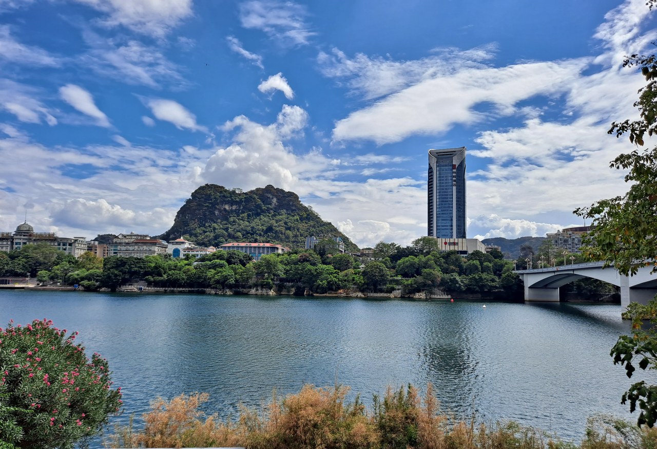 A wooded limestone hill rises beside water and modern buildings in Liuzhou.