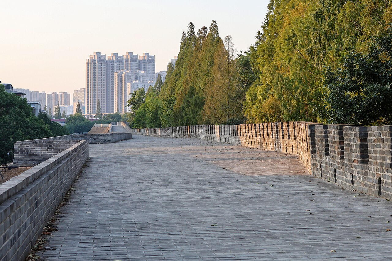A wide stone walkway along Xiangyang’s city wall, with trees and modern buildings beyond.