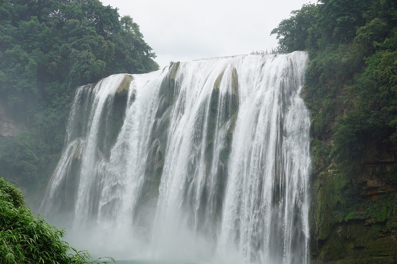 Huangguoshu Waterfall descending over a broad rock face between green slopes.