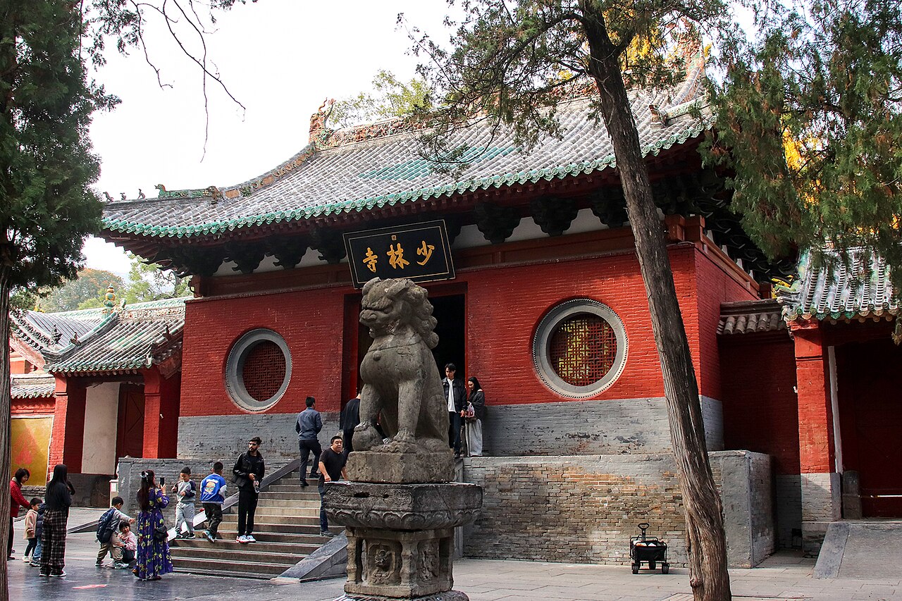 Shaolin Temple’s red mountain gate, grey tiled roof and stone lion beneath tall trees.