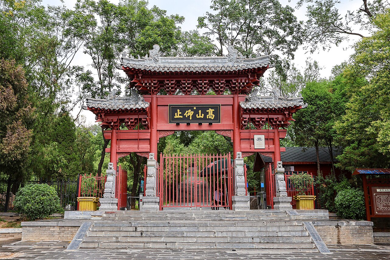 Songyang Academy’s red ornamental entrance framed by green trees, with stone steps in front.