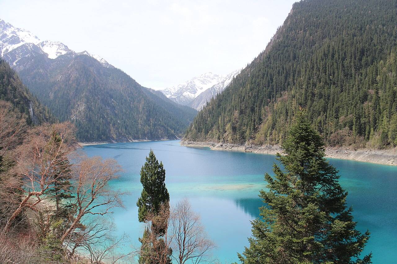 Blue Long Lake stretches between forested slopes toward snow-covered mountains.