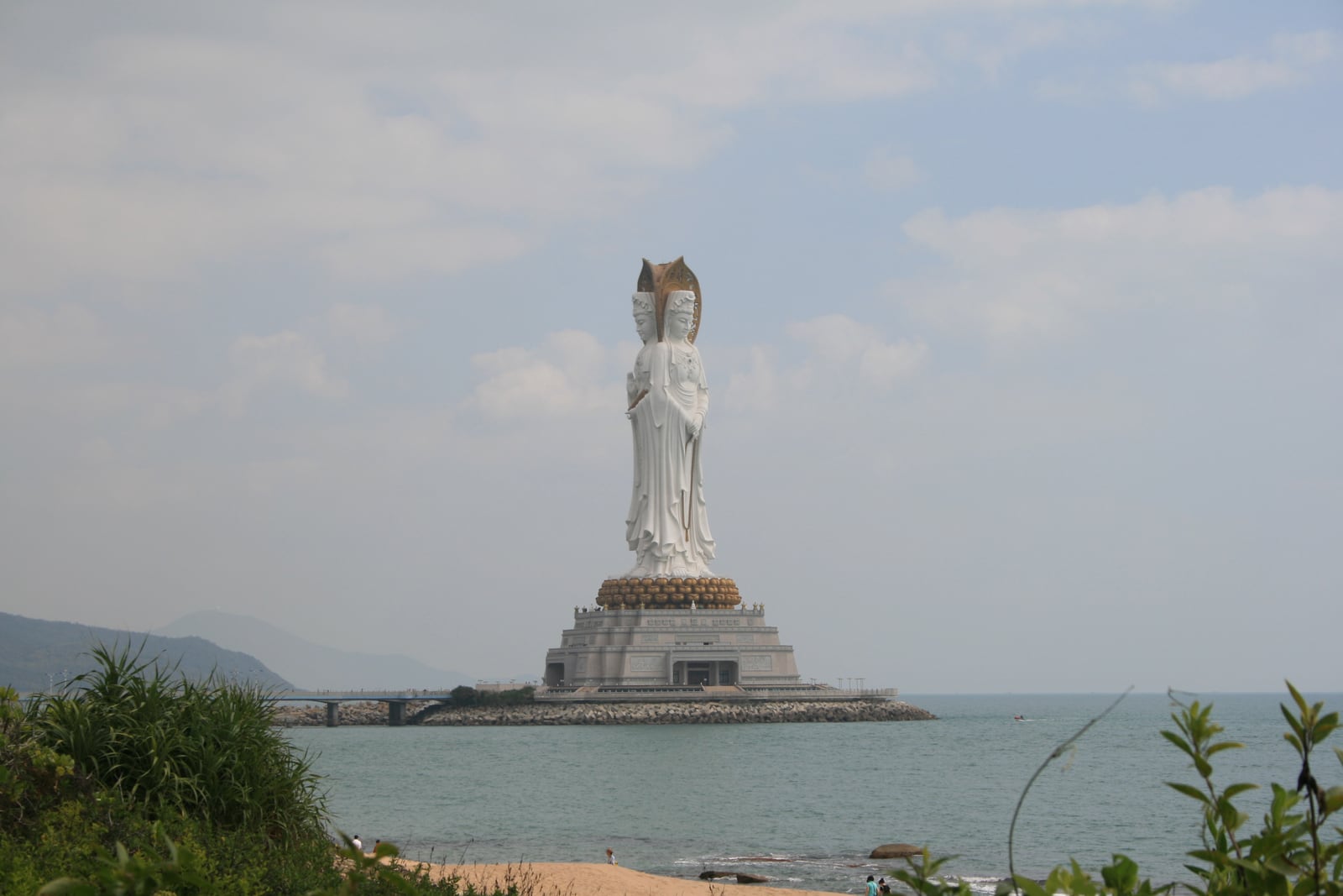 The white Guanyin statue stands on its offshore platform at Nanshan, with the coastal approach visible