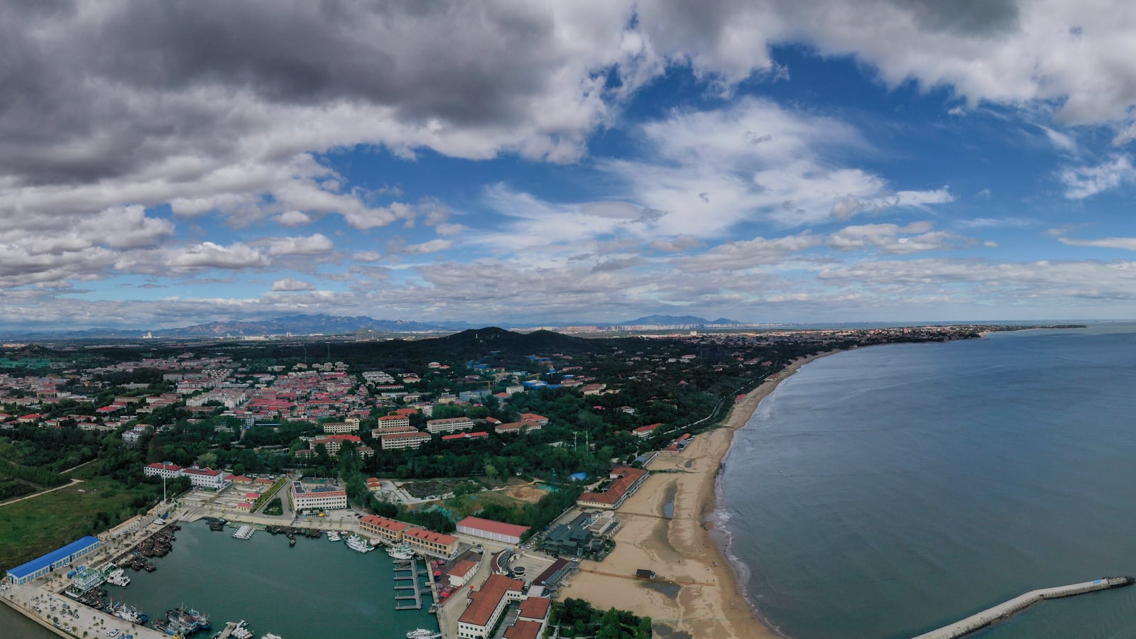 Beidaihe coastline curving past wooded hills and low buildings, viewed north from above the Dai River.