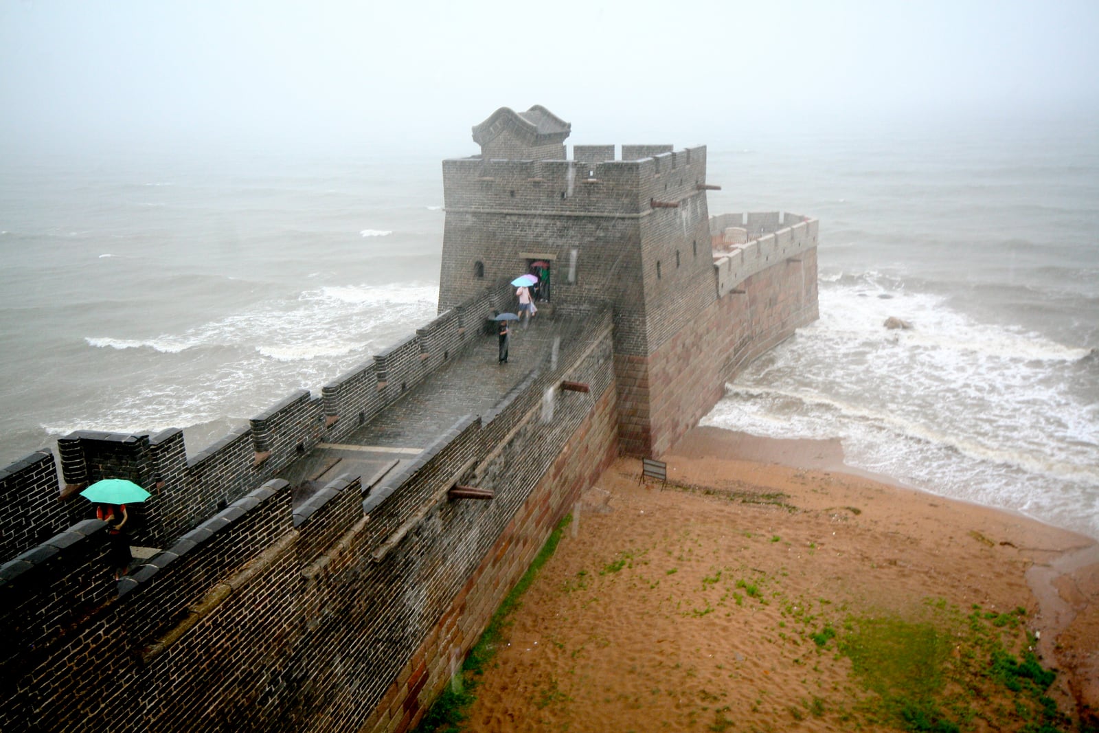 Stone fortifications at Old Dragon Head project into the sea, with the visitor walkway and sandy shore alongside.
